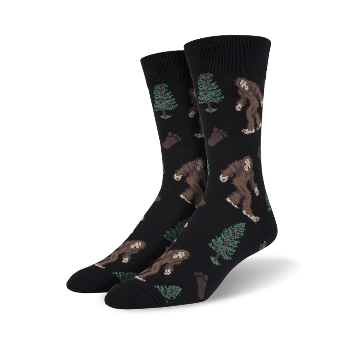 Pair of crew socks; black background with brown Bigfoot, green trees, and brown footprints. Fun, whimsical design.