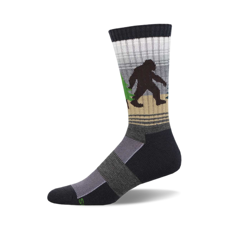 Crew socks in dark gray, beige, and white, featuring a Bigfoot walking through a forest. Green trees and a subtle striped pattern.