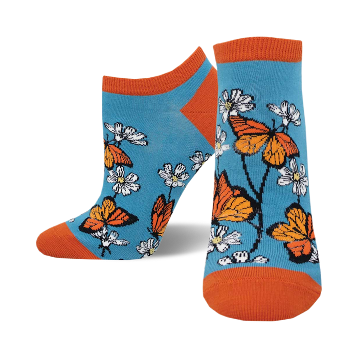 the socks have an all-over pattern of orange butterflies and white and yellow flowers on a blue background. the butterflies and flowers are arranged in a repeating pattern. the socks have an orange cuff at the top. }}