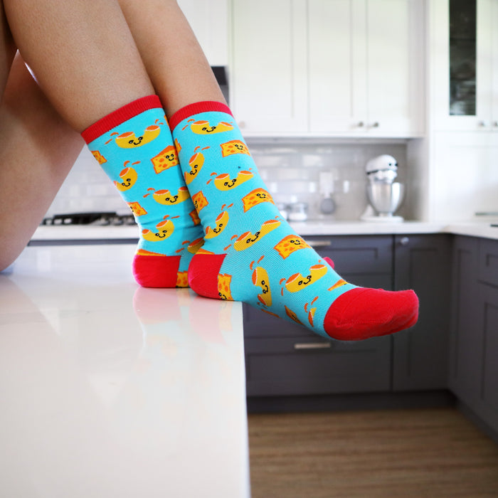 Lifestyle photo of Mac N Cheese socks on a person's legs, set in a kitchen.