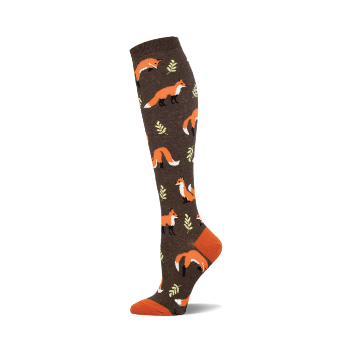 A brown knee-high sock with a repeating pattern of orange foxes and small green leaves. The toe and cuff are a contrasting burnt orange. }}