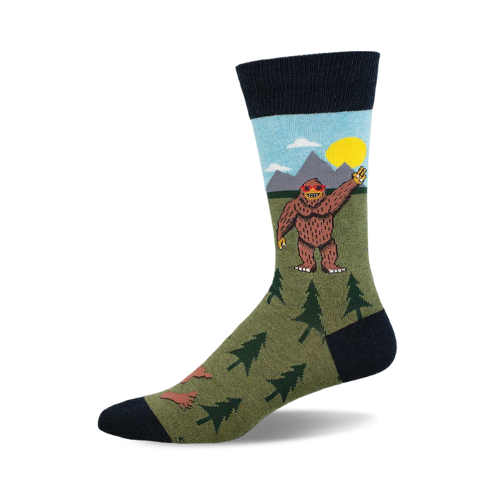 Crew socks in olive green, navy blue, and light blue, featuring a cartoon Bigfoot waving, mountains, and little trees. }}