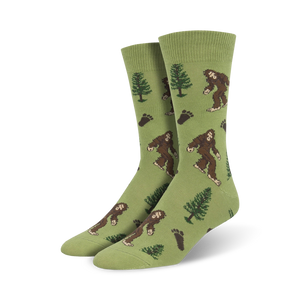 Lifestyle shot of a person's feet wearing a pair of olive green Bigfoot XL crew socks.  The socks feature a pattern of Bigfoot, trees, and footprints.