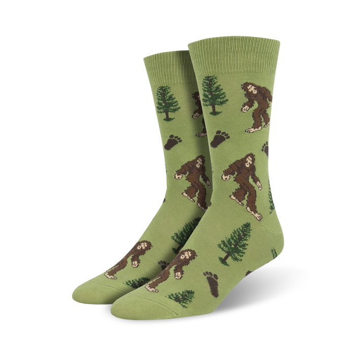 Lifestyle shot of a person's feet wearing a pair of olive green Bigfoot XL crew socks.  The socks feature a pattern of Bigfoot, trees, and footprints.