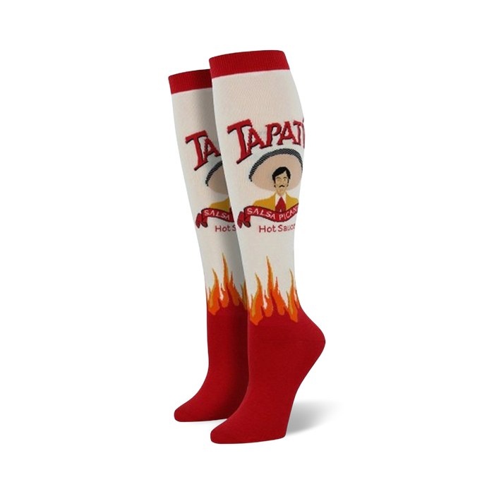 Pair of cream and red knee-high socks. Features a Tapatio hot sauce bottle design, including the brand logo, mascot, and flames. }}