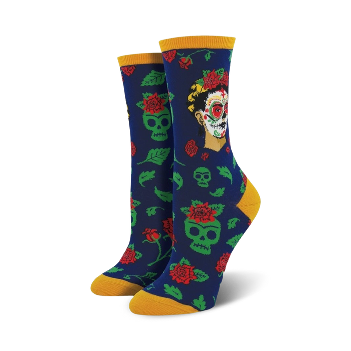 A pair of women's crew socks in navy blue. The socks feature a pattern of green sugar skulls, red roses, and a portrait of Frida Kahlo styled as a Catrina. }}