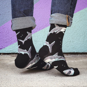 A person is modeling a pair of black socks with a pattern of cartoon sharks. The socks are pulled up to the person's calves and the person is wearing blue jeans.