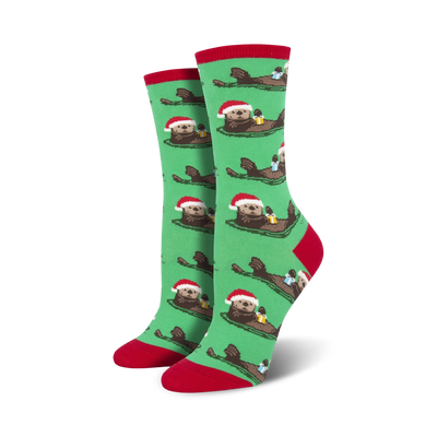 Pair of women's crew socks. Green background with repeating pattern of otters wearing Santa hats and holding gifts. Red and teal accents.