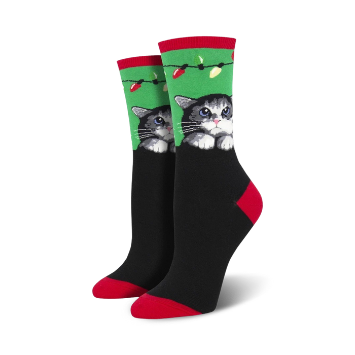 Pair of women's crew socks. Black background, green and red accents, cute gray cat peeking over the top with holiday lights.