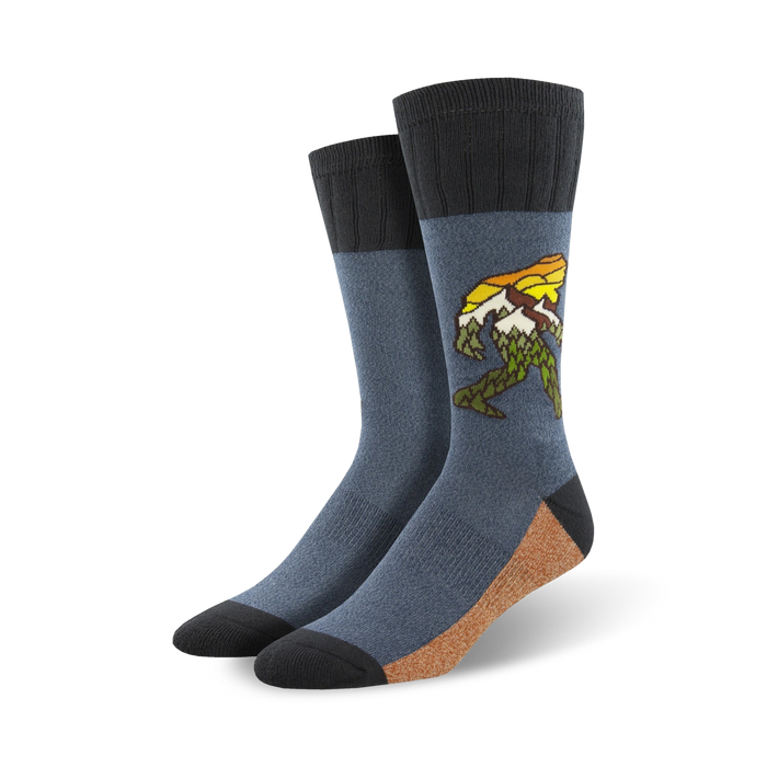 A pair of men's crew socks in blue and tan, featuring a graphic of Bigfoot walking through a mountain range.  The design includes yellow and green accents. }}
