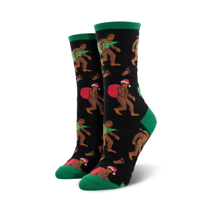 A pair of women's crew socks with a black background. Bigfoot characters wear Santa hats and carry Christmas trees. Green cuffs and red accents. }}