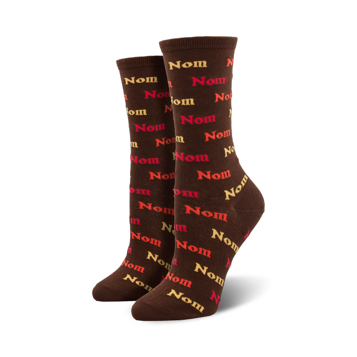 Pair of brown crew socks with a repeating pattern of the word 'Nom' in shades of red, orange, and beige. }}