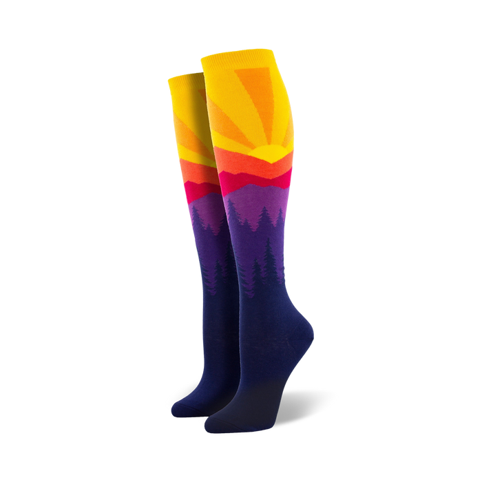 Pair of women's knee-high socks showcasing a vibrant sunset over silhouetted mountains. Colors include yellow, orange, red, purple, and navy blue. }}