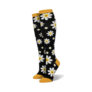 Pair of black knee-high socks with white smiling daisy pattern and mustard yellow cuffs.