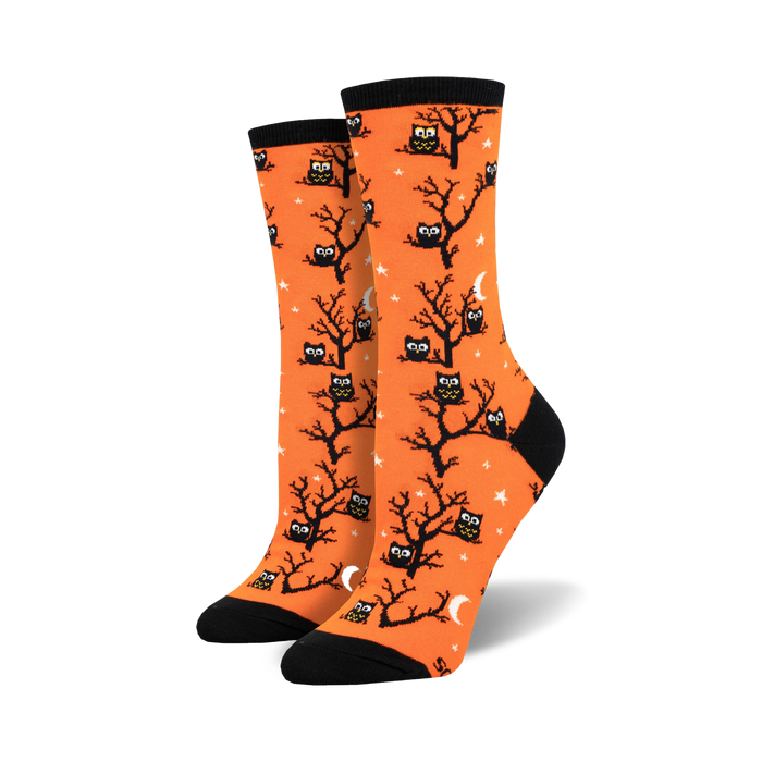 A pair of women's crew socks in bright orange. The socks are covered in a pattern of black owls sitting in bare trees against a background of small white stars and crescent moons.