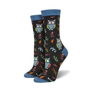 Close-up of a pair of black crew socks with owls, leaves, and berries. Blue top trim.