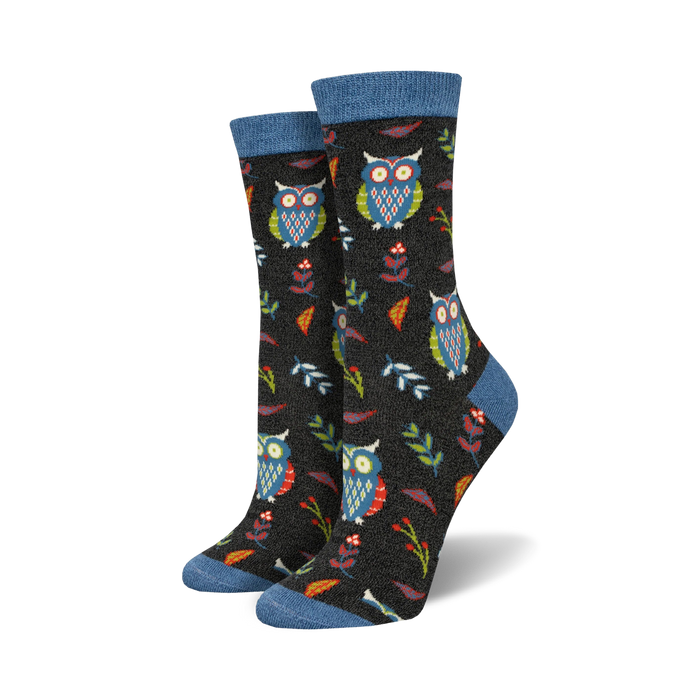 Close-up of a pair of black crew socks with owls, leaves, and berries. Blue top trim.