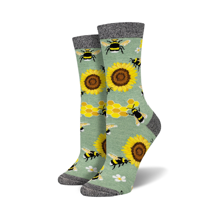 Pair of crew socks with bees, sunflowers, and honeycomb pattern on a sage green background.  Black and grey top cuff.