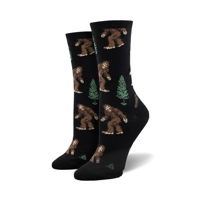 Pair of women's crew socks. Black background with repeating pattern of brown Bigfoot figures and green evergreen trees. }}