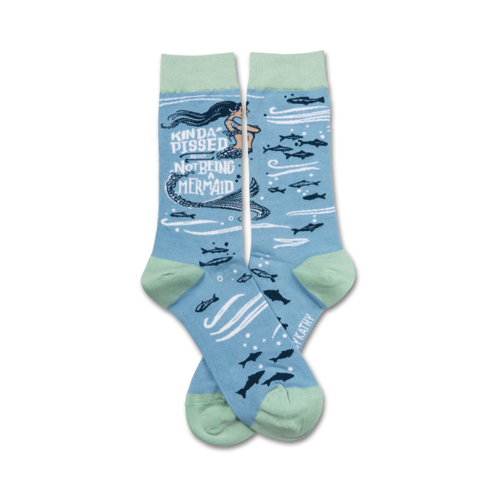 A pair of crew socks in light blue and mint green. The design features a cartoon mermaid with the text 'Kinda Pissed About Not Being a Mermaid' and small fish. }}