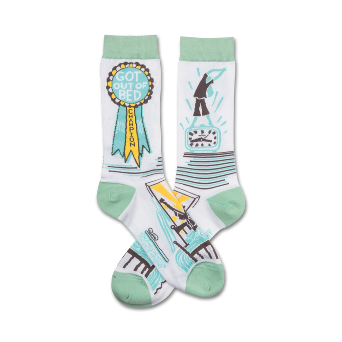 Pair of white crew socks with mint green cuffs. One sock features a 'Got Out of Bed Champion' ribbon; the other shows a figure jumping out of bed next to a clock. }}