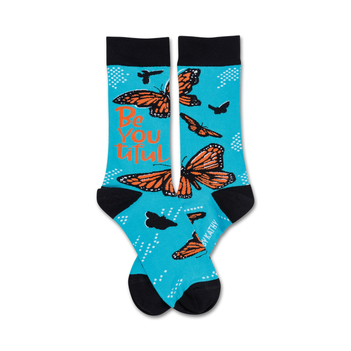 A pair of turquoise crew socks with orange monarch butterflies and the text 'Be You Tiful'. Black cuffs and small white dots complete the design. }}