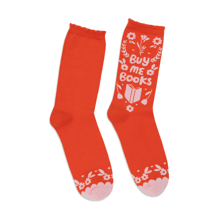 A pair of orange crew socks with a whimsical 'Buy Me Books' design in white and pink. Features floral accents and a book graphic. }}
