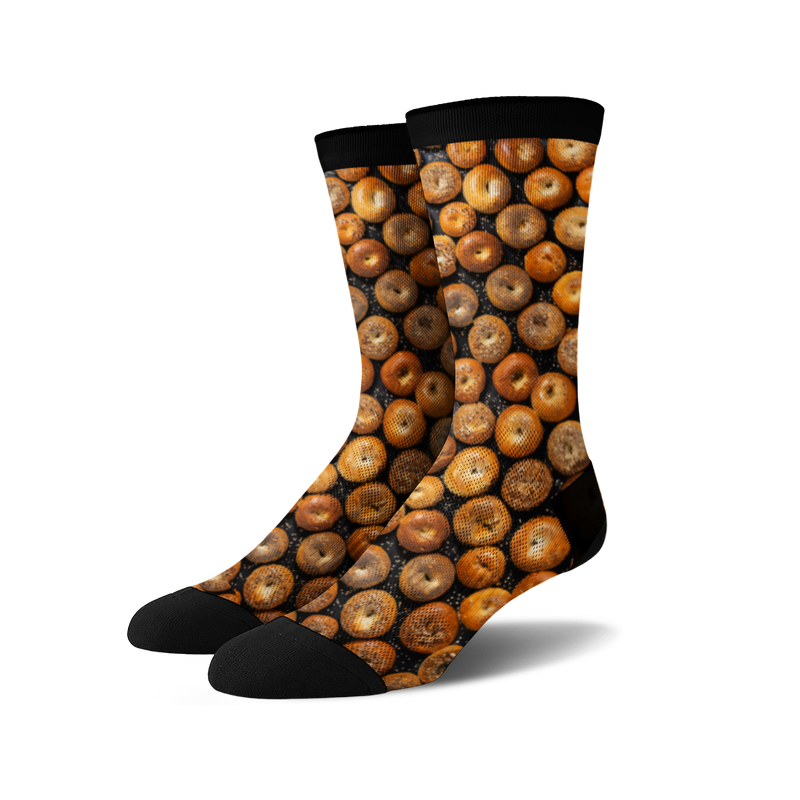 A pair of crew socks with a full-coverage print of various bagels in shades of brown and tan on a black background.
