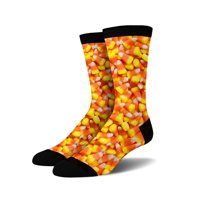 A pair of crew socks covered in a candy corn print. The socks are predominantly orange, yellow, and white, with a black cuff.