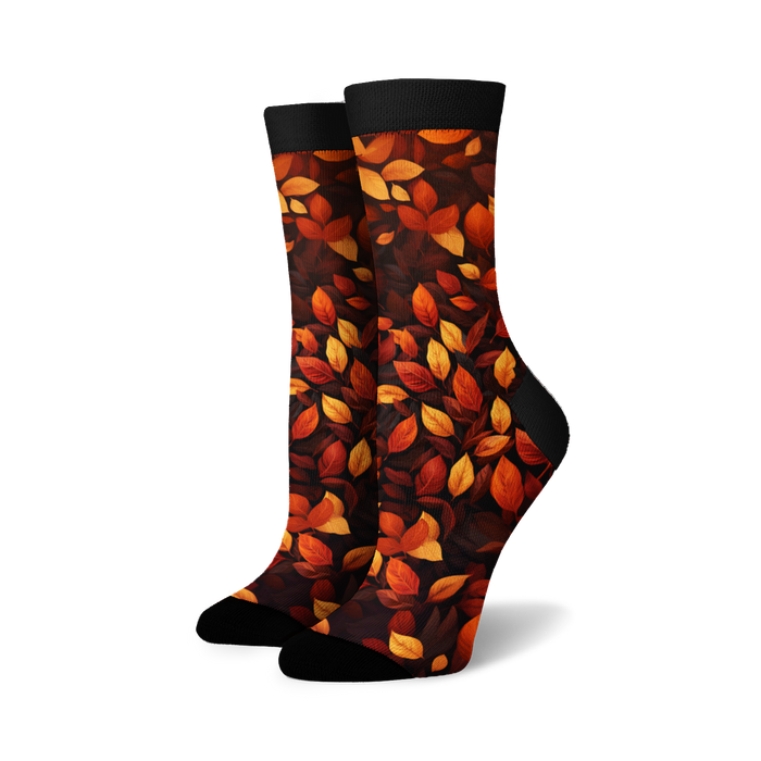 A pair of crew socks with an allover pattern of autumn leaves in orange, red, yellow, and brown on a black background.