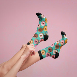 A pair of donut socks are displayed against a pink backdrop, with a person's hands pulling up one of the socks.