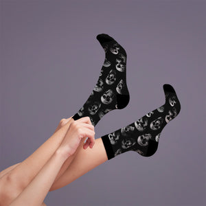 Lifestyle shot: a person adjusting the black skull socks on their legs.