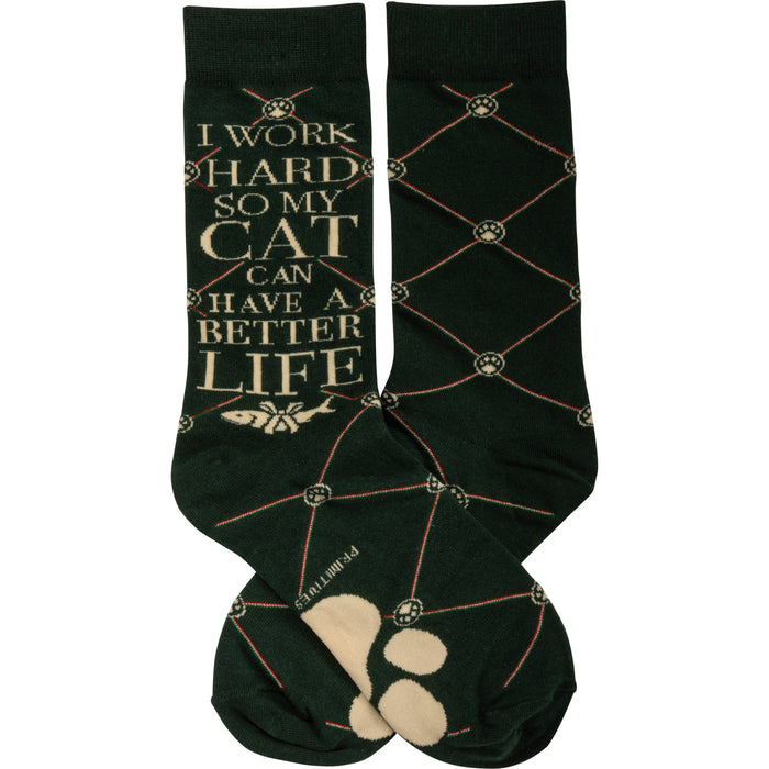 Pair of dark green crew socks. One sock features the text 'I work hard so my cat can have a better life' and a small fish image. A repeating paw print and crisscross pattern is visible on both socks. }}