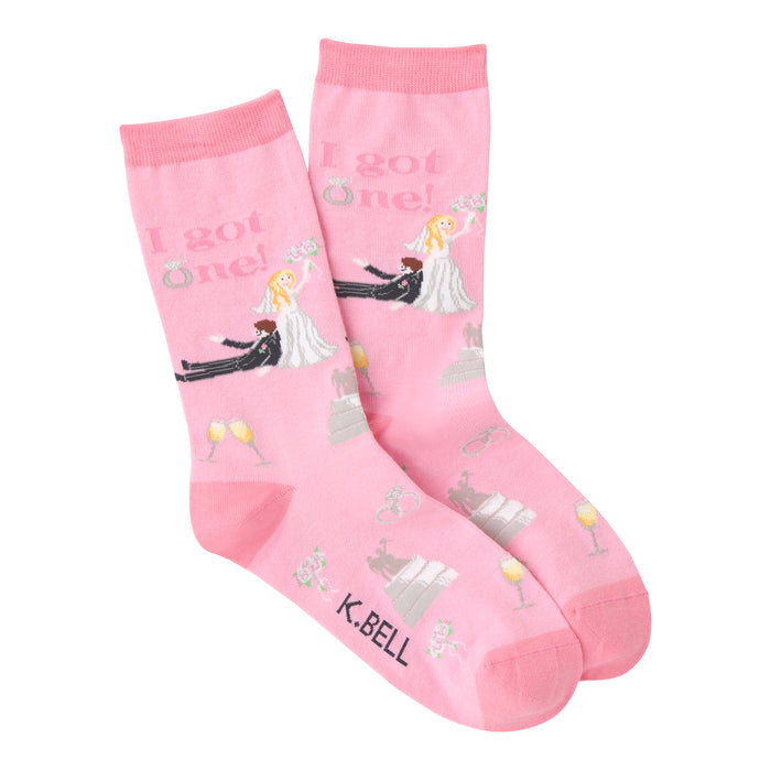 A pair of pink crew socks. The socks have a wedding theme with illustrations of a bride and groom, rings, cake, and champagne glasses. Text reads: 'I got one!' }}
