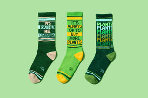 Product shot of three different gardening-themed socks: 'I'd Rather Be Gardening', 'It's Always Ok To Buy More Plants', and 'Plants Plants Plants'.