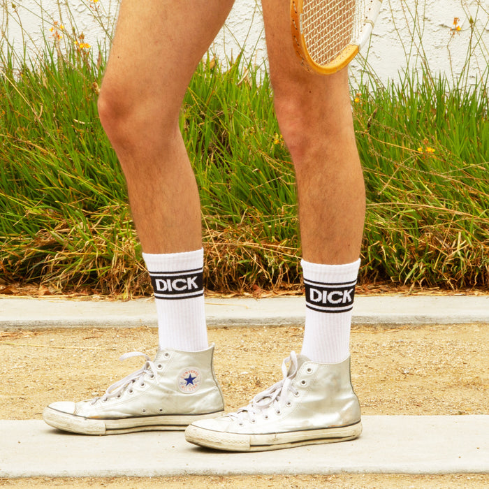 Lifestyle shot: Close-up of legs wearing 'Dick' socks and silver Converse sneakers.