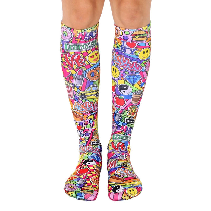 Knee-high socks in pink, yellow, and other bright colors. Features a fun, collage-style design of NYC imagery like smiley faces, pizza, and traffic lights.