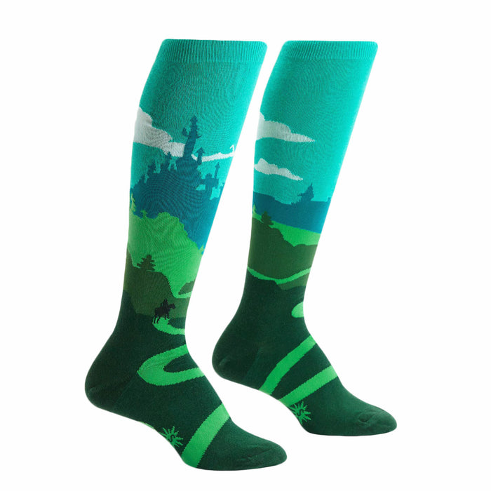 Pair of teal and green knee-high socks depicting a whimsical landscape with a castle, winding road, and a moose. }}