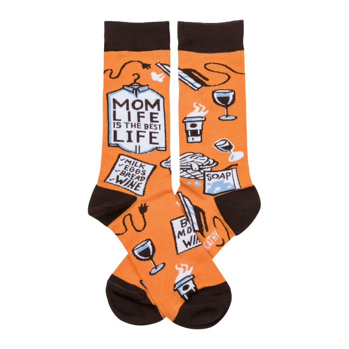 A pair of orange crew socks with a brown cuff. The socks show illustrations of coffee, wine, laundry, and a shopping list that says 'Mom Life is the Best Life'. }}