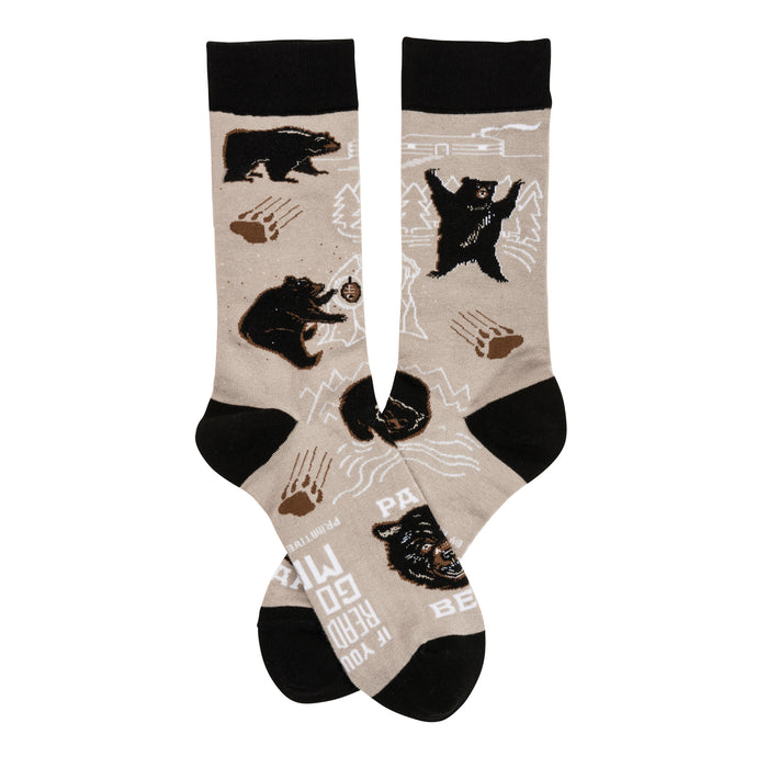 A pair of beige crew socks with a playful design featuring black bears, paw prints, and mountain outlines. The cuffs are black. }}
