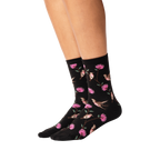 Lifestyle shot of woman's legs wearing black crew socks with hummingbird pattern.