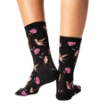 Back view of a pair of black crew socks with a hummingbird and flower pattern.