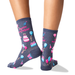 A pair of gray socks with a colorful pattern of birthday-related items, including balloons, presents, hats, and cakes.