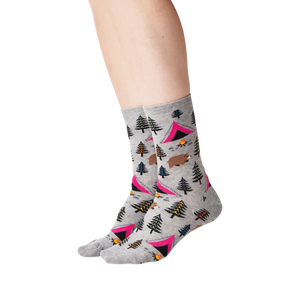 A pair of gray socks with a pattern of pink tents, green and blue pine trees, brown bears, orange campfires, and yellow and blue mountains.