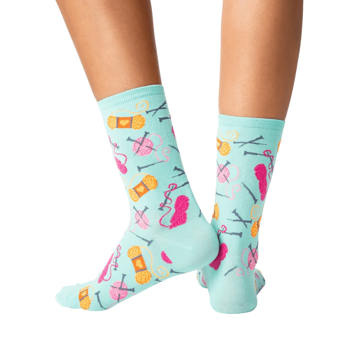 A pair of light blue socks with a pattern of knitting needles and yarn in pink, orange and red.