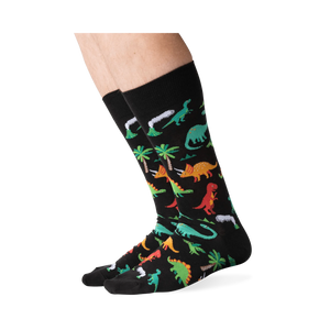 Lifestyle shot showing the dinosaur socks on a person's legs against a green background.