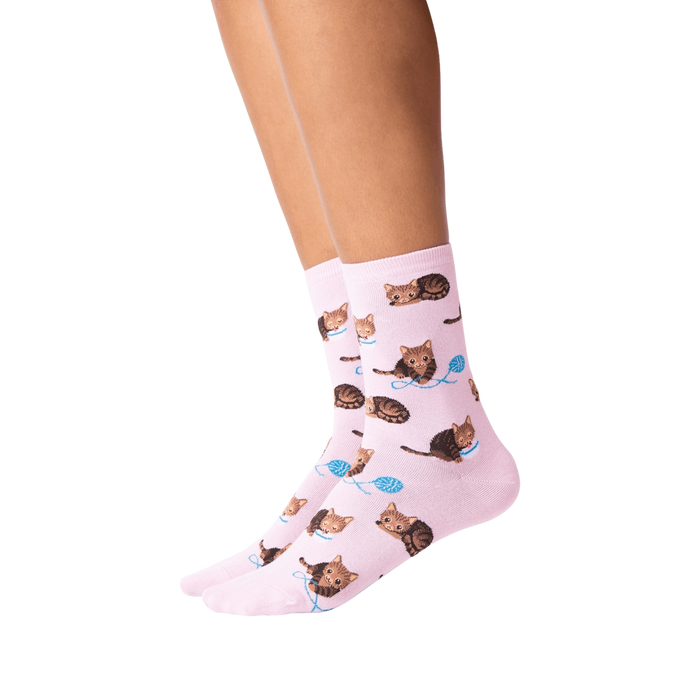 A pair of pink socks with a pattern of brown tabby cats playing with blue yarn balls.