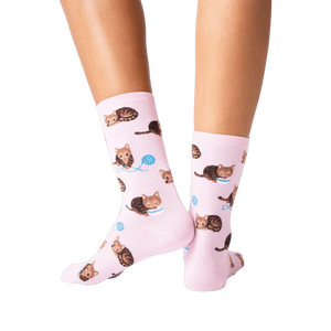 Back view lifestyle shot: Person's legs wearing pink socks with a repeating pattern of brown cats and yarn.