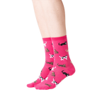 Lifestyle shot showing a person wearing a pair of pink Classic Cats socks. The socks are crew length and feature a pattern of various cats in black, brown, and white.