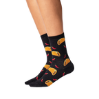 Lifestyle shot showing the socks on a person's legs. They're black with a taco and chili pepper pattern.